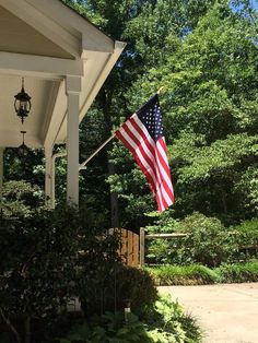 an american flag flying on the front porch of a house with trees in the background