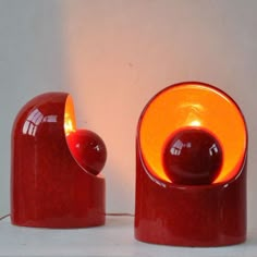 two red vases sitting next to each other on a white counter top with an orange light in the middle