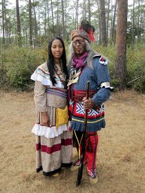 two people dressed in native american clothing standing next to each other on a dirt ground