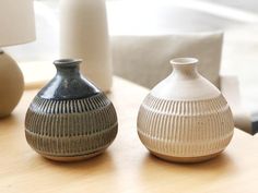 two vases sitting on top of a wooden table next to each other, one white and the other gray