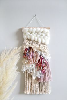 a wall hanging made out of yarn and wool balls on a white background next to a dried plant