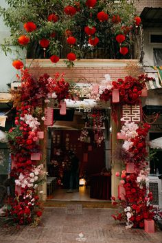 red and white flowers are hanging over the entrance to a building with an open door