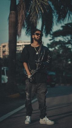 a man standing on the side of a road next to a palm tree and wearing sunglasses