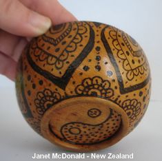 a hand is holding a wooden ball with an intricate design on the outside and inside