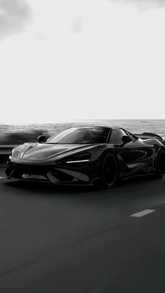 a black and white photo of a sports car driving on the road by the ocean