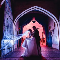 a bride and groom standing in front of an archway at their wedding reception with the veil blowing in the wind