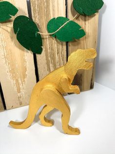 a wooden toy dinosaur standing in front of a wood fence with green leaves on it