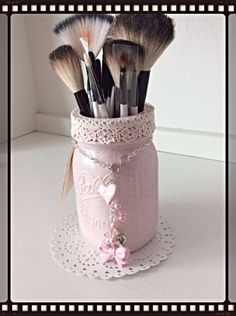 a jar filled with lots of makeup brushes on top of a doily covered table