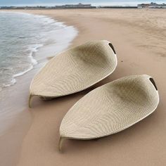 two oval shaped baskets sitting on top of a sandy beach next to the ocean,