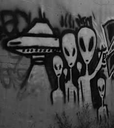 black and white photograph of graffiti on the side of a wall with three alien heads