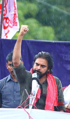 a man holding a microphone up in the air while standing next to another man with an umbrella