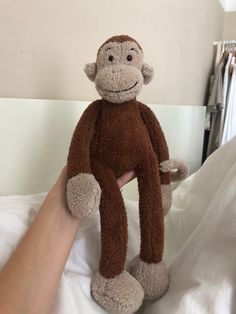 a hand holding a stuffed monkey on top of a bed