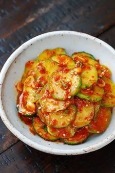 a white bowl filled with zucchini and tomato sauce on top of a wooden table