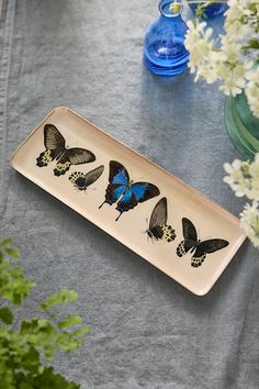 a plate with butterflies on it next to some white flowers and blue glass vases