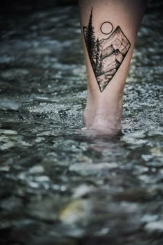 a person's foot in the water with mountains and trees tattoo on their leg