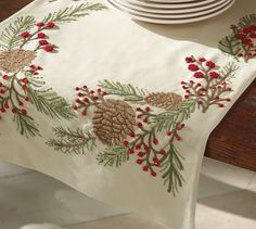 a white table cloth with pine cones and red berries on it, next to plates