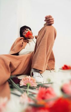 a person sitting on the ground with flowers in their lap and one hand holding a flower