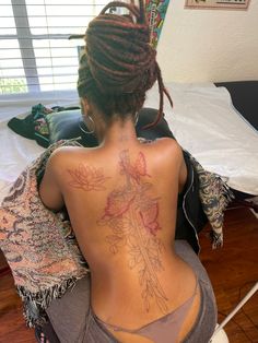 a woman sitting on a bed with her back turned to the camera and tattoos on her body