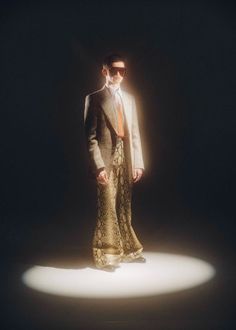 a man in a suit and tie standing on a dark background with light coming from behind him