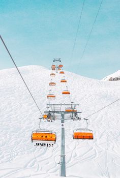 a ski lift going up the side of a snow covered mountain with orange chairs on it