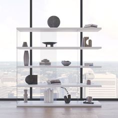 a white shelf with books and vases on it in front of a large window