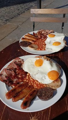 two plates with eggs, sausages and beans on them sitting on a wooden table