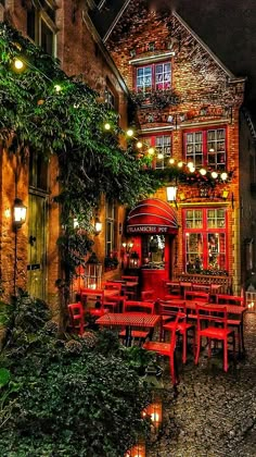 an outdoor restaurant with red chairs and tables in front of the building at night time