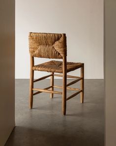 a chair made out of wicker sitting on top of a cement floor next to a white wall