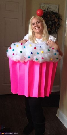 a woman standing in front of a giant pink cupcake with sprinkles on it