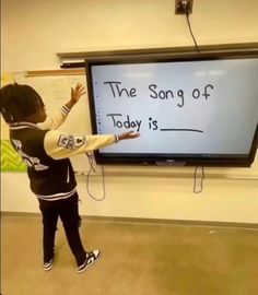 a young child standing in front of a large screen with the words the song of today is written on it