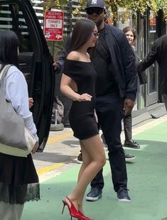 a woman in black dress and red high heels standing next to a man wearing a suit