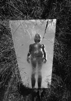 a person standing in front of a mirror with grass around it and the reflection of them