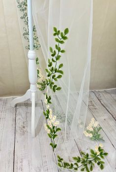 white flowers and greenery are on the floor next to a sheered window curtain