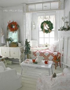 a living room filled with white furniture and christmas wreaths on the window sill