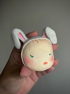 a hand holding a small ceramic animal with bunny ears on it's head and eyes