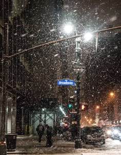 two people are standing on the street corner in the snow at night with traffic lights