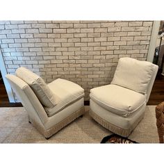 two chairs sitting next to each other in front of a brick wall with a cat laying on the floor