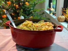 a red pot filled with macaroni and cheese on top of a table next to a christmas tree