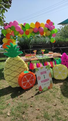 a table topped with lots of fruit under a colorful arch filled with balloons and decorations