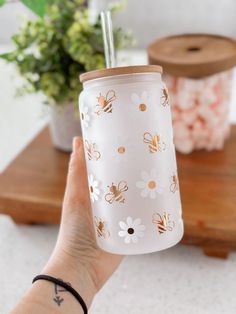 a person holding up a glass cup with flowers on it and a straw in the bottom