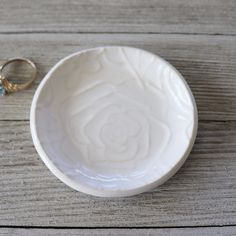 two wedding rings are placed in a white bowl next to the ring holder on a wooden table