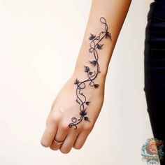 a woman's wrist tattoo with vines and flowers on the left side of her arm