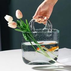 a person is holding a clear bag with flowers in it and goldfish swimming inside