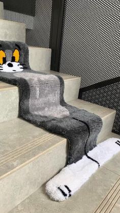 the cat rug is on the stairs next to the handrails and has yellow eyes