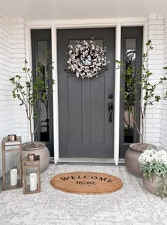 a welcome mat on the front door of a house with potted plants and lanterns