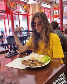 a woman sitting at a table in front of a plate of food with chopsticks