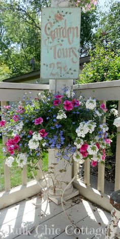 a sign that says garden tours on the side of a porch with flowers in it