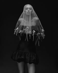 a woman with a veil on her head wearing a black dress and heels in front of a dark background