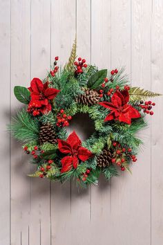 a christmas wreath with poinsettis and greenery hanging on a wooden wall