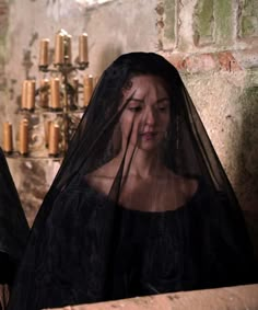 two women dressed in black veils standing next to each other with candles on the wall behind them